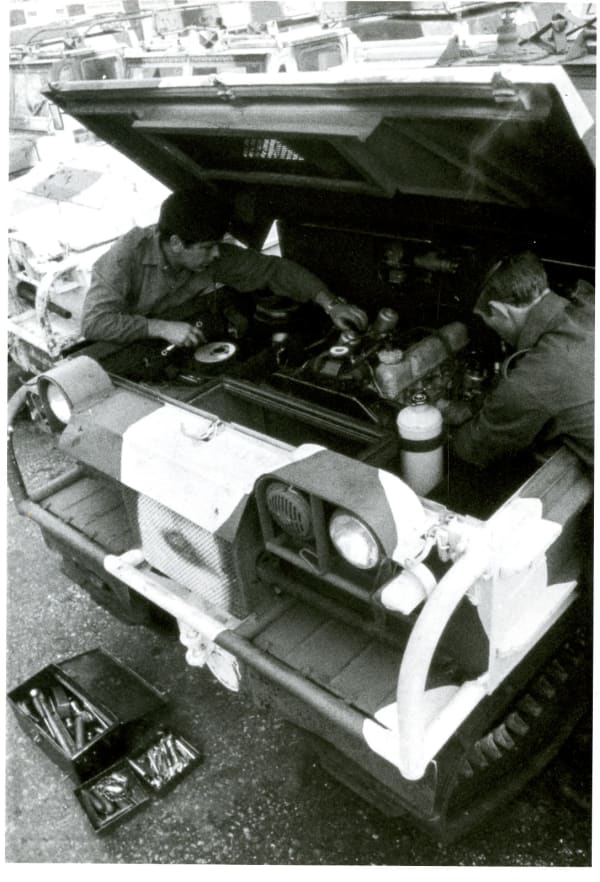 Soldiers working under the bonnet of a vehicle, other vehicles visible next to it, toolbox on the floor.