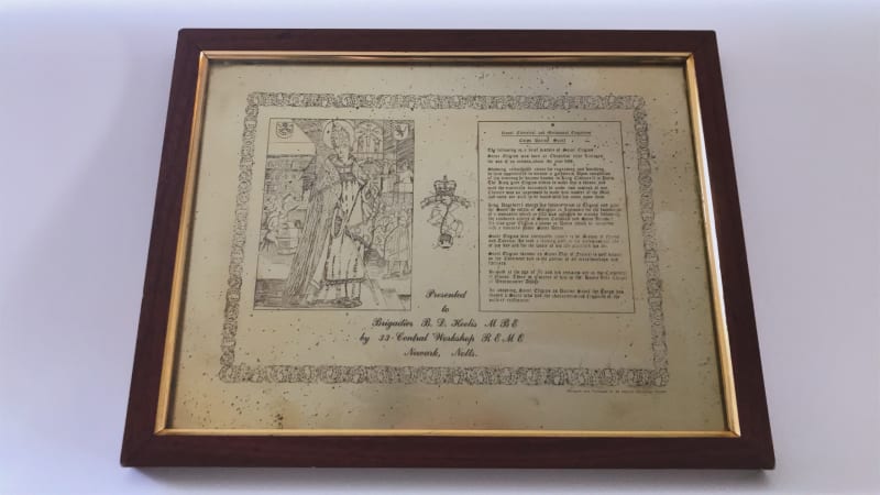 Framed picture of a saint and accompanying story in black and white. The frame is brown wood with a gold strip. 