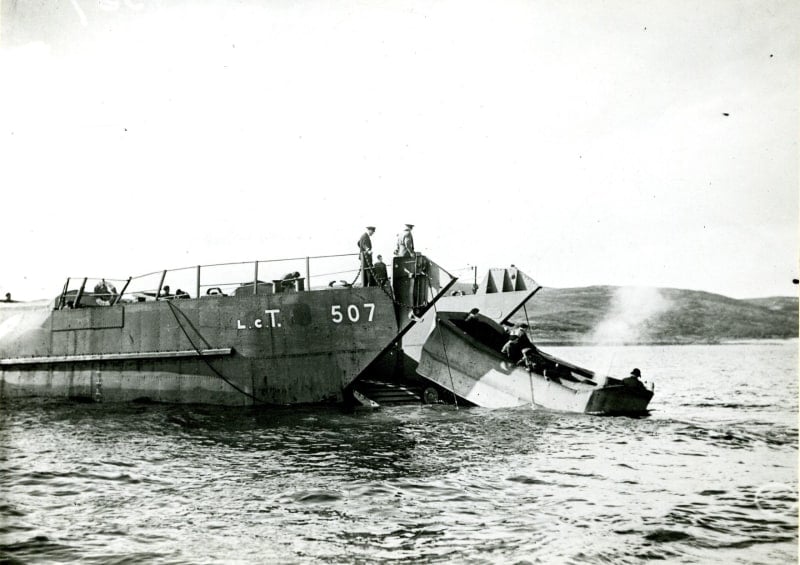 A landing craft with door open and a small vehicle being launched into the water.