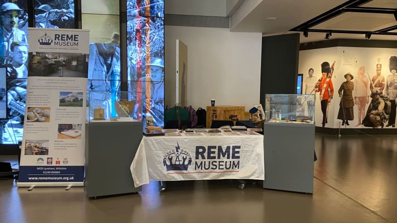 A table with white tablecloth reading REME Museum, in between two display cases and a pop up banner on the left. 