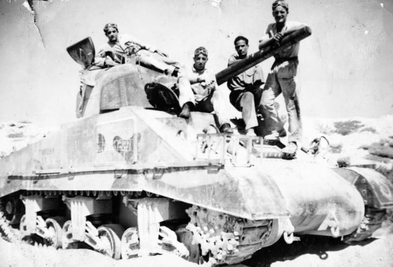 Black and white photograph of a tank, side on, with 4 crewmen standing on top.
