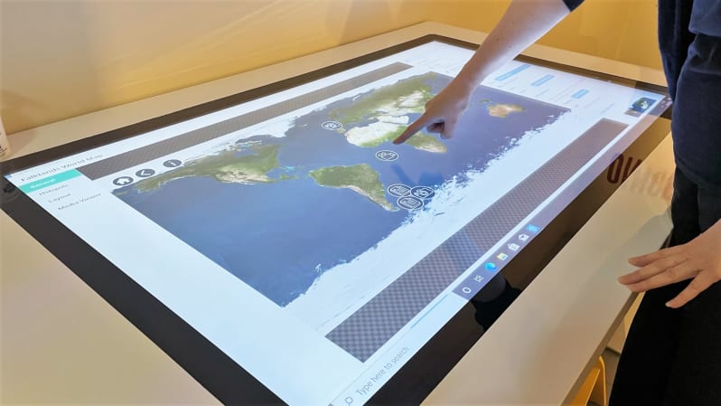 Image shows someone pointing at a world map on a large screen