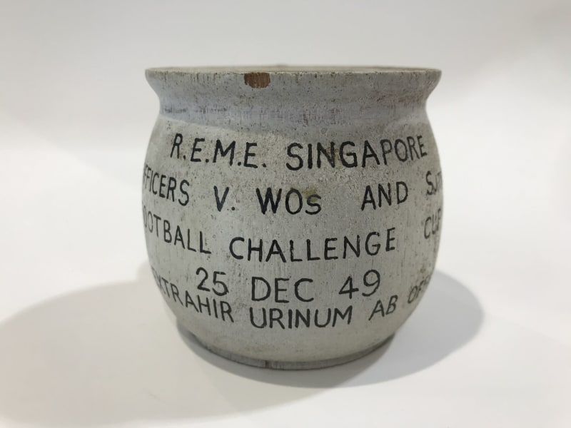 Stone chamber pot with black text on the front. Text reads " R.E.M.E. Singapore, Officers V WOs and S..., Football Challenge Cup, 25 Dec 49, Nil xxtrahir urinum ab officious " .