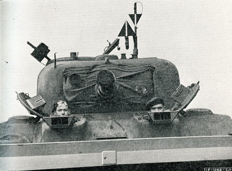 A tank turret with two soldier poking their heads out of the top on both sides. 