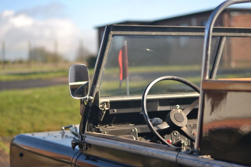 View of the front half of the car with steering wheel, windscreen and mirror in view. 