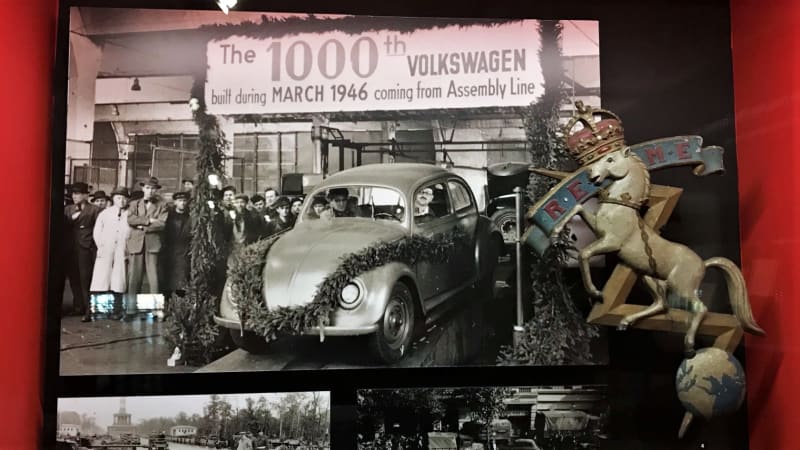 REME crankshaft cap badge in a display case in front of a photograph of the Wolfsburg VW factory