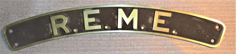 Metal nameplate with gold lettering and border and black background. The plate is slightly curved and reads "R.E.M.E.".