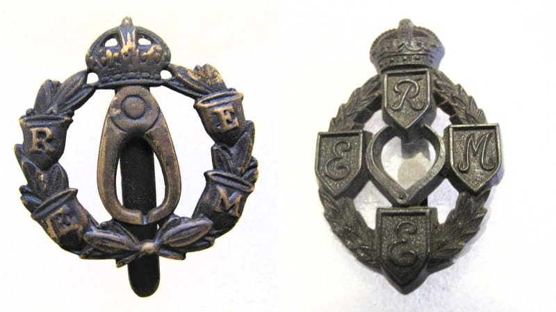 Two dark metal cap badges side by side, each with similar features of callipers, crown and letters but in different variations.
