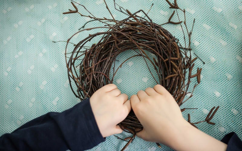 Image shows the hands of a child holding a wreath of willow branches