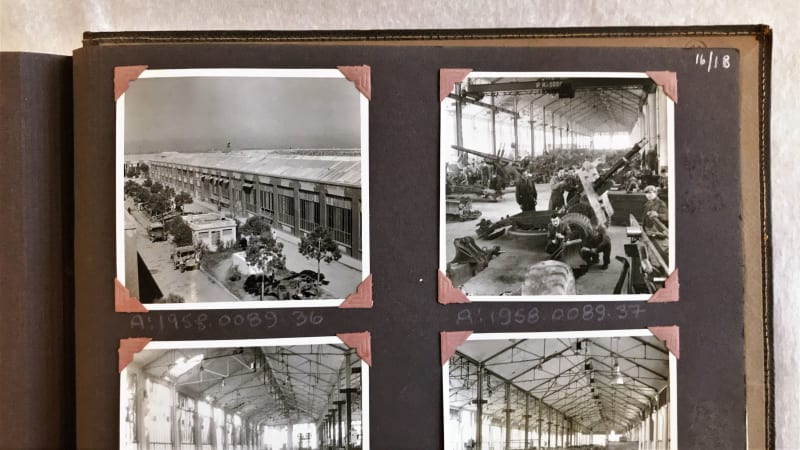 Four black and white photos stuck in a book with black paper. Top left photo shows a factory from the outside. Top right photo shows an artillery gun being made. Bottom two photos cut off.