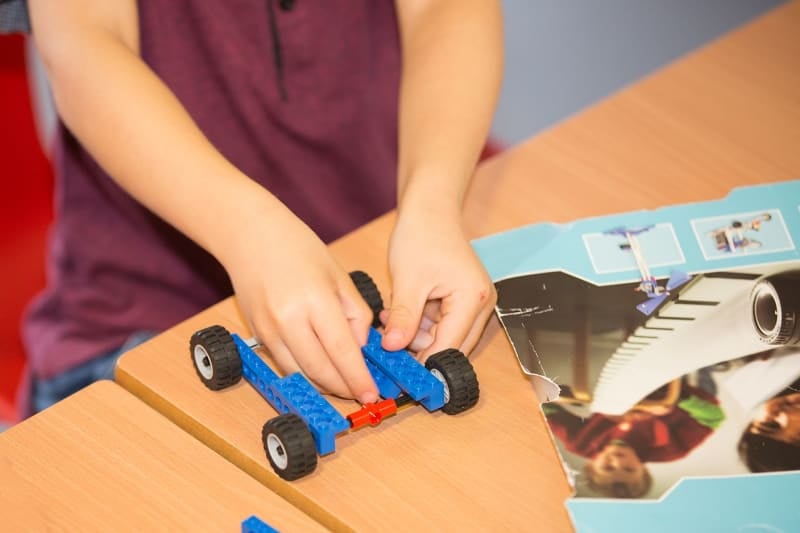 Image shows the hands of a child fixing LEGO bricks onto a LEGO car. 