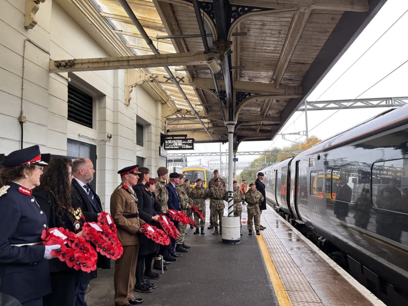 People stood in a line on a train platform holding poppy wreaths.