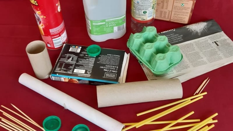 Assortment of recyclable materials on red background. Materials shown are cardboard boxes and tubes, a milk carton, newspaper and paper straws.