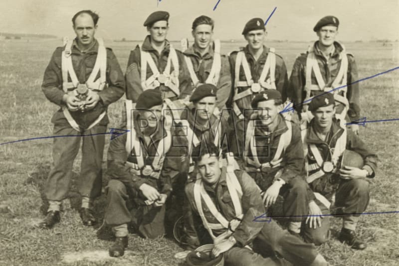 Image shows a group photograph of men wearing parachute harnesses.