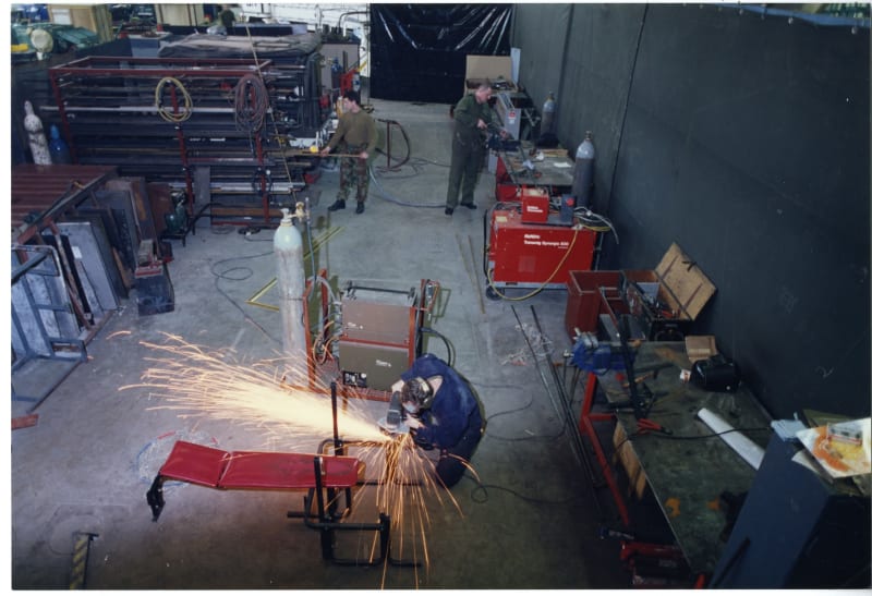 Image shows a view from above of a metalsmith in a workshop. Sparks are flying out from where they are cutting metal.