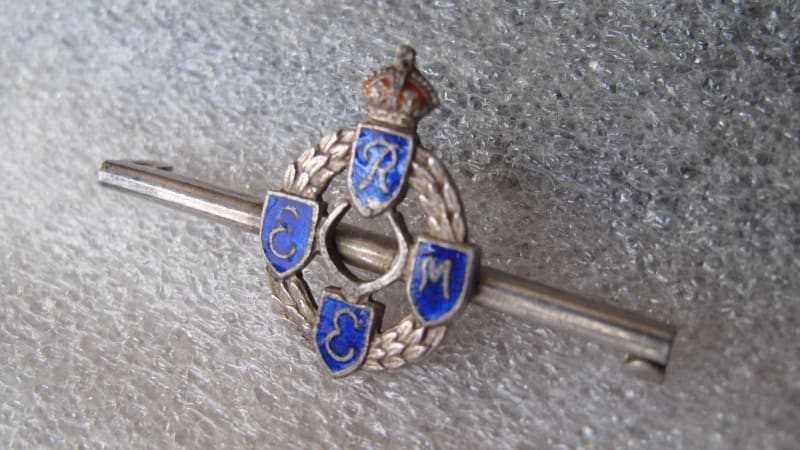 First pattern REME badge, silver with blue shields and gold and red crown, on a silver bar perpendicular to the badge at the back.