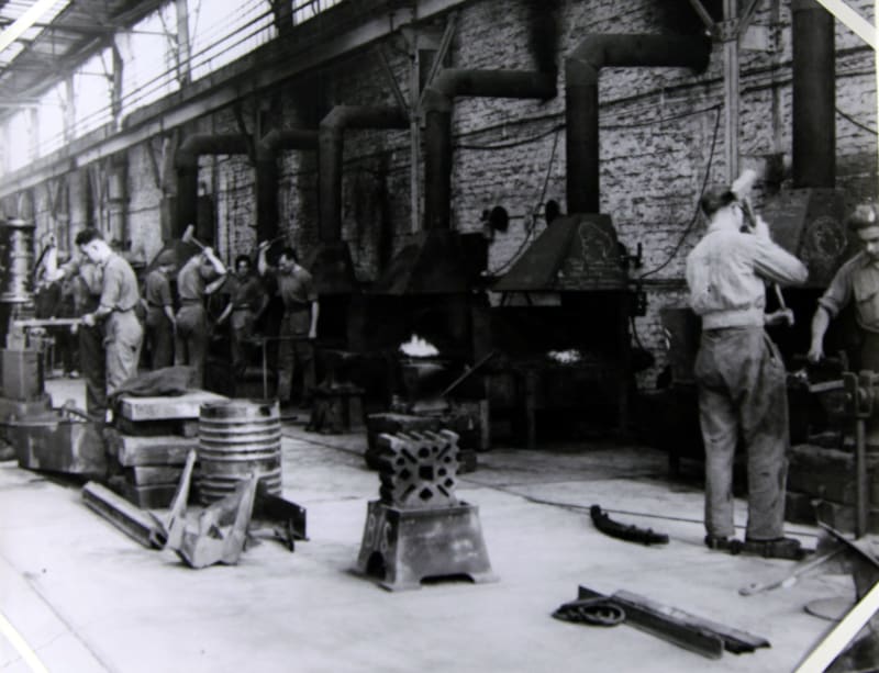 Image shows a black and white photograph of metalsmiths working inside a workshop.