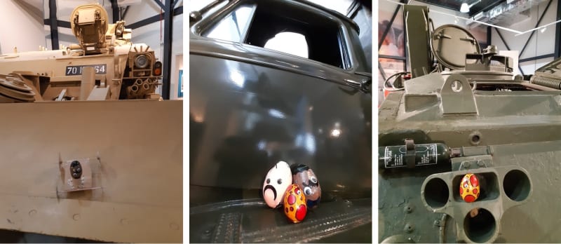 Three images. From left to right, the first is an egg painted black on a model chariot rolling down the flat surface of a military vehicle. The second image is a close up of a group of eggs, two with faces painted and one with yellow and red spots. They sit on the door of a car. The last image is a red and yellow spotted egg in the gun of a large green tank.