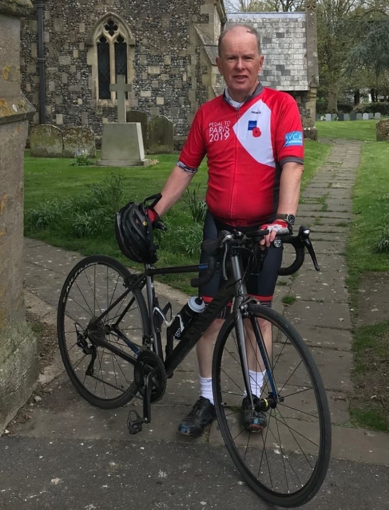 Steve in red cycling jersey stands with bike in churchyard.