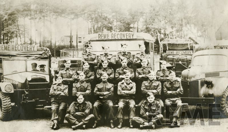 A black and white group photograph of soldiers in front of three trucks.