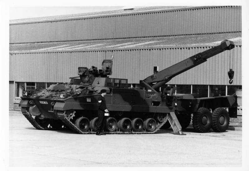 A large tracked armoured vehicle with crane outside a building.