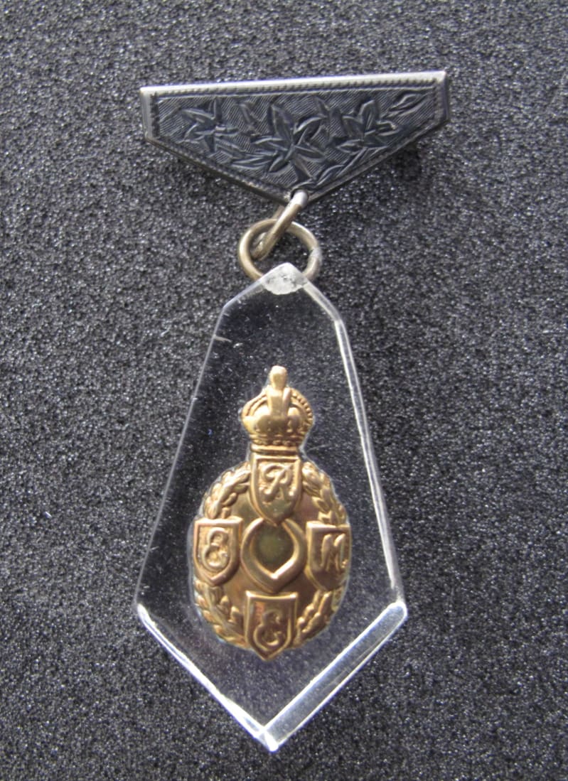 Clear plastic diamond shaped pendant with gold coloured first pattern REME badge in centre, small rings attached to top.