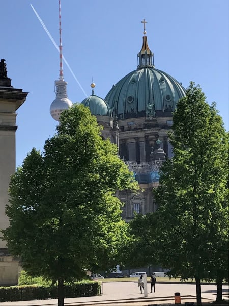 Top of Berlin Cathedral behind two trees. Two people walk below.
