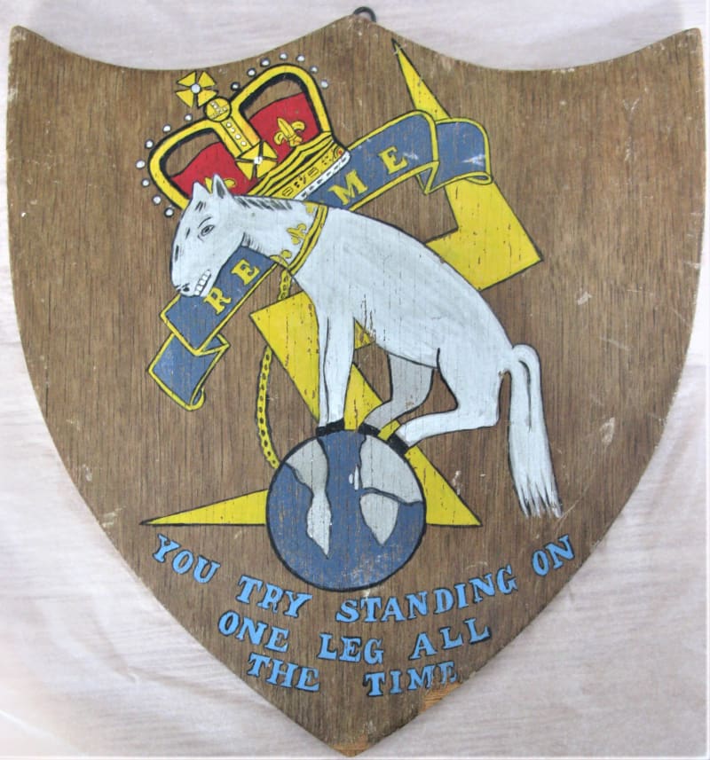 A wooden shield-shaped plaque with cartoon of a tired horse stood on the globe with lightning behind and a crown. Blue writing reads "You try standing on one leg all the time".