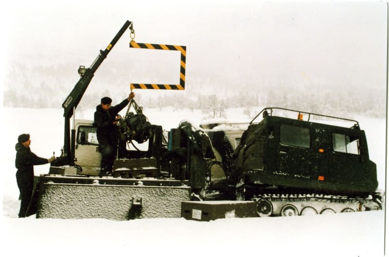 Soldiers and a crane lifting an engine out of a vehicle in snow.