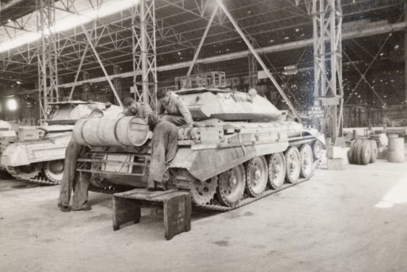 Black and white photograph of a tank with several people working on it at one end. 