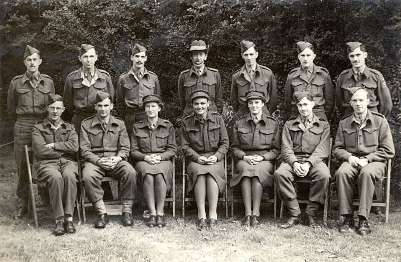 Black and white photo of male and female officers in uniform. Seven sit at the front and seven stand behind. All look at camera.