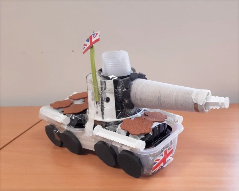 A model tank made out of recycled plastics and materials. Printed British flags stuck on the front and atop a straw sticking upwards.