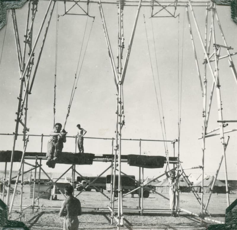 A scaffolded structure with 2 harnesses attached, 2 men stood and sat on the structure, another stands on the floor looking up.