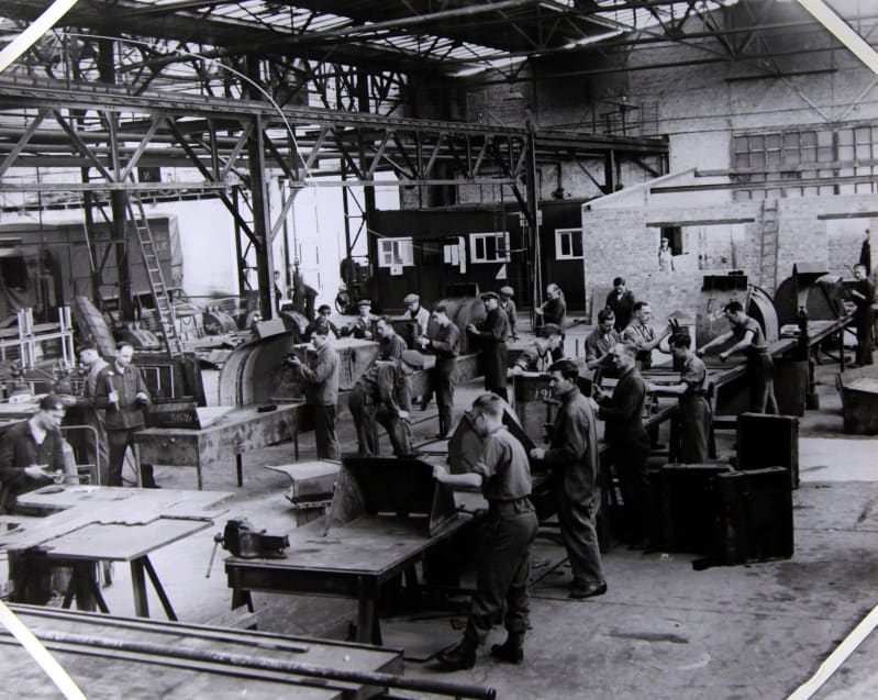 Image shows a black and white photograph of metalsmiths working inside a workshop.