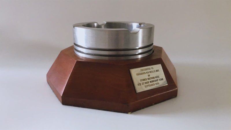Silver metal ashtray on top of a brown hexagonal base. On one side of the base is a rectangle with a presentation engraving.