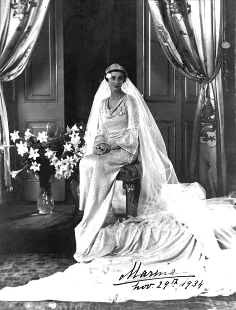 Black and white photograph of Princess Marina sitting in a white wedding dress and veil, train laid out in front. Signed at the bottom in black ink.