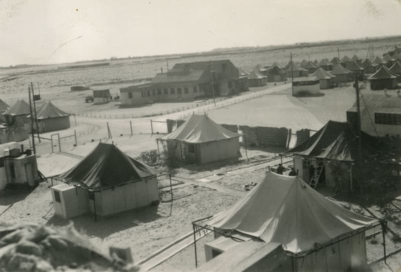 A black and white photo of tents and buildings in a landscape.