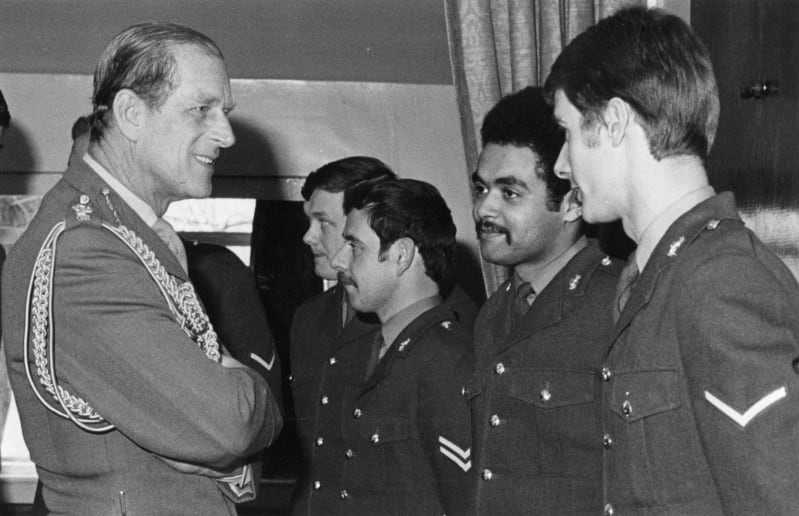 Black and white photograph of Prince Philip talking to soldiers in a line. All wear uniform.