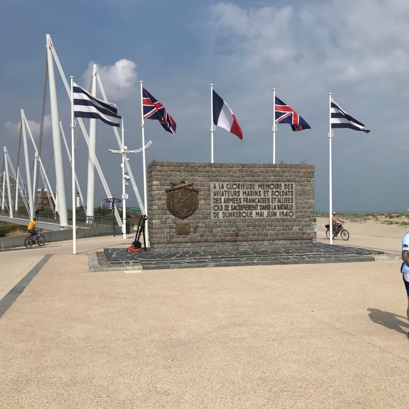 Image shows the memorial on Dunkirk Beach with flags behind it