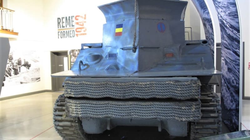 Front view of a large armoured vehicle, grey, with ropes attached to the front in horizontal lines.
