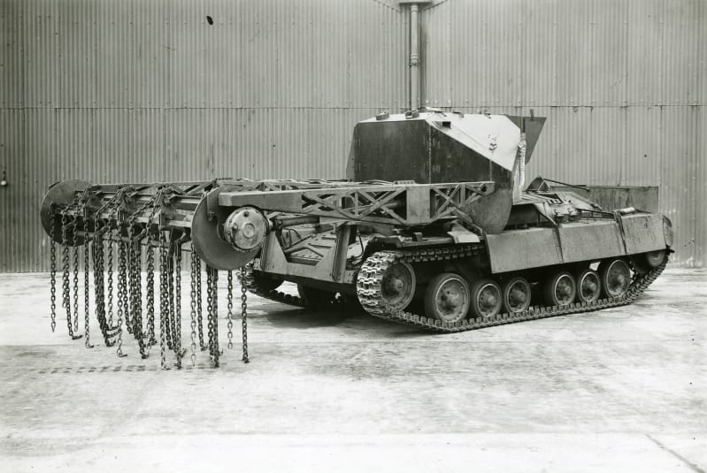 Black and white photo of a tank from a diagonal front perspective, with rotating attachment fixed onto crane at front, chains attached to the rotator.
