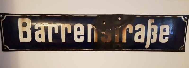 Metal street sign that reads " barrenstrasse " in white and showing damage from two bullet holes.