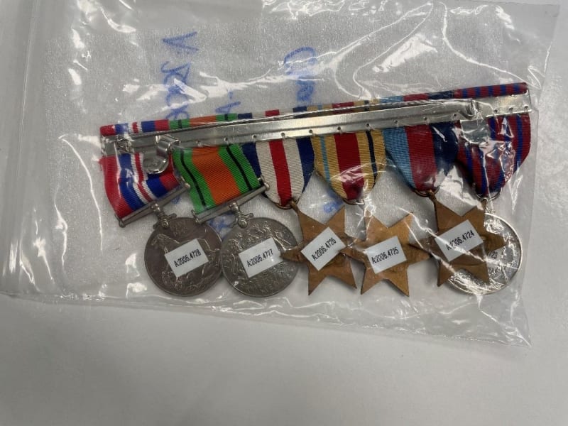 Six medals inside a clear plastic bag, stickers with a series of numbers and letters are on the metal