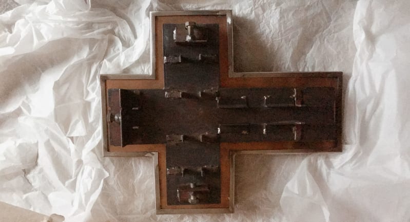 A wooden cross shape with metal parts inside and clamps to hold materials in.