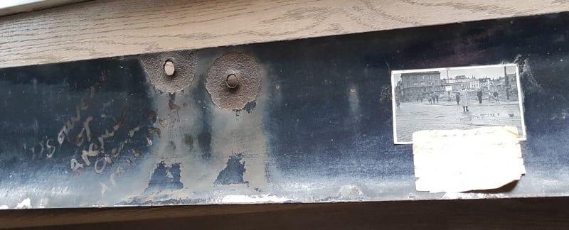 Back of a street sign. A note and a black and white photograph of people in a city are attached on the right. Bullet holes are visible.