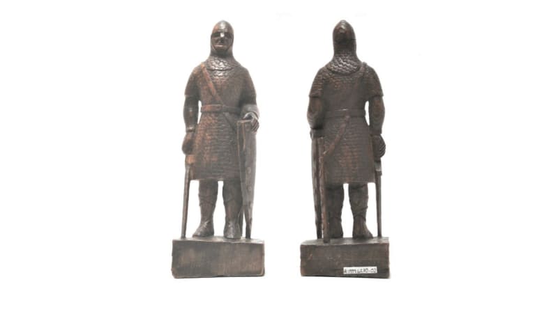 A wooden sculpture of a knight holding a sword downwards and a shield on a plinth, two perspectives from the front and back, on a plain white background.